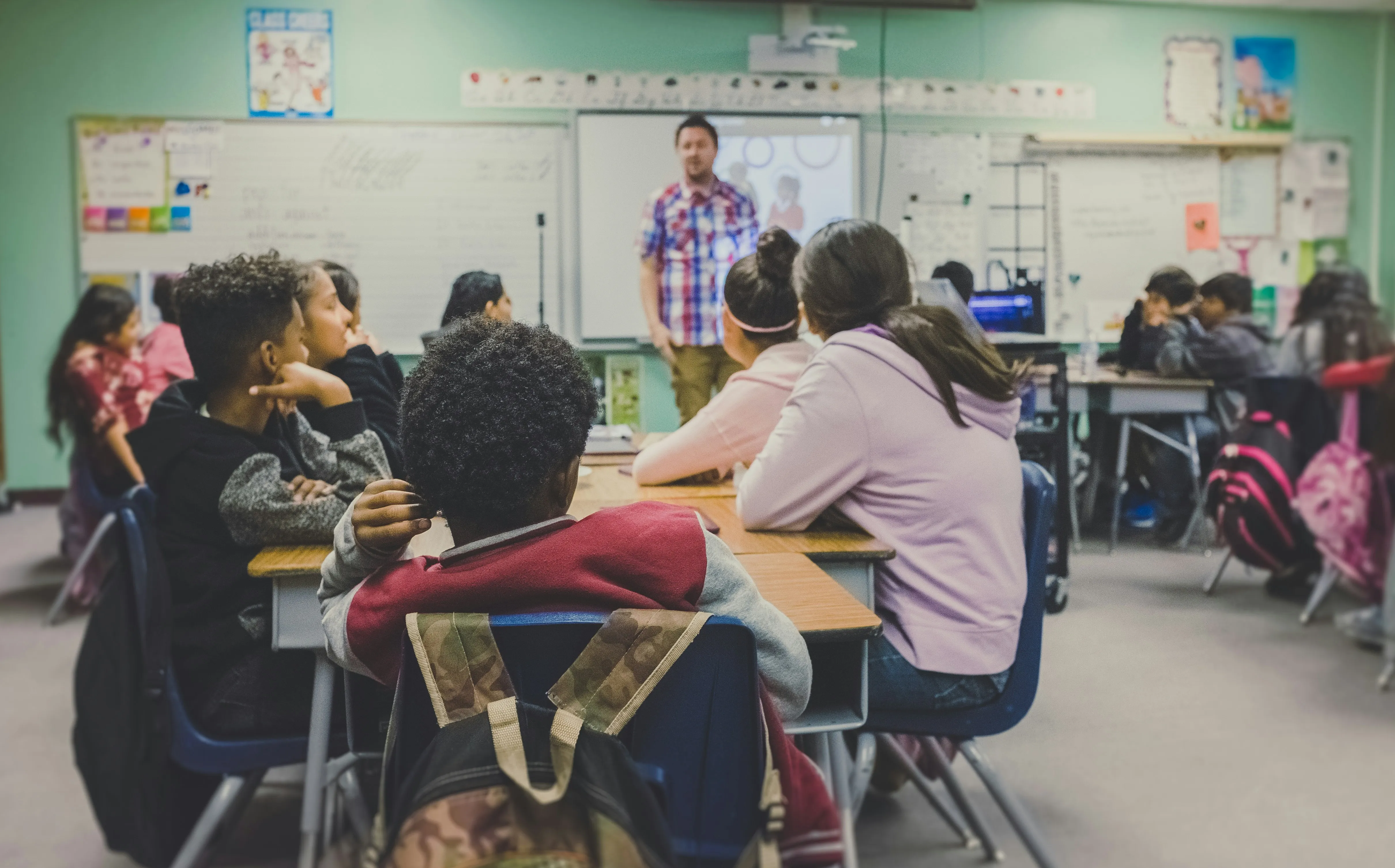 A teacher stands at the front of a classroom, delivering a lesson to a group of students.